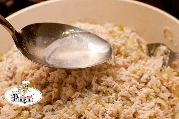 A spoon with broth over a bowl with onions, celery, and minced chicken meat